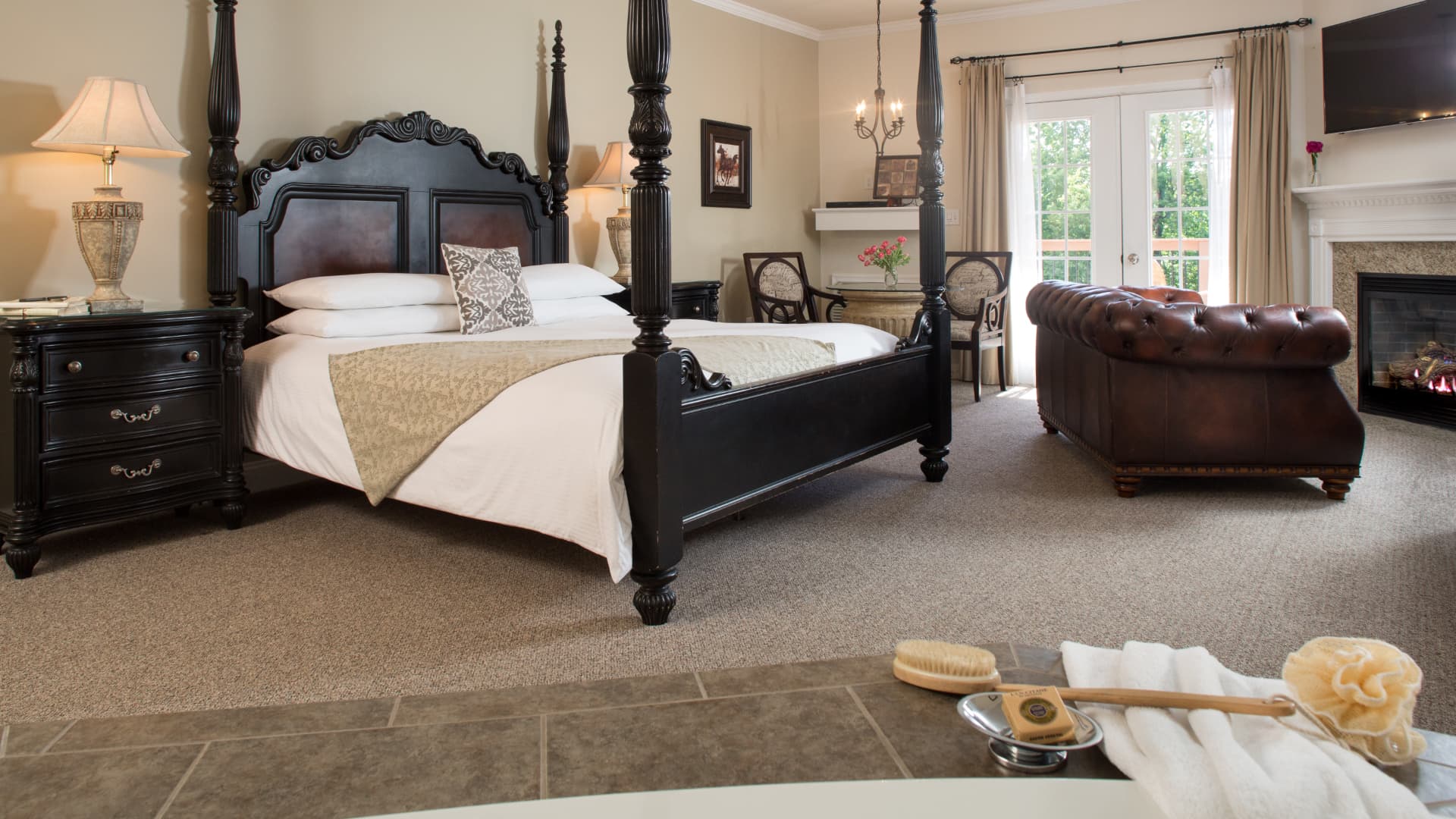 A luxurious, spacious bedroom with a 4-poster bed, sofa, fireplace, table and chairs in the corner, and tub