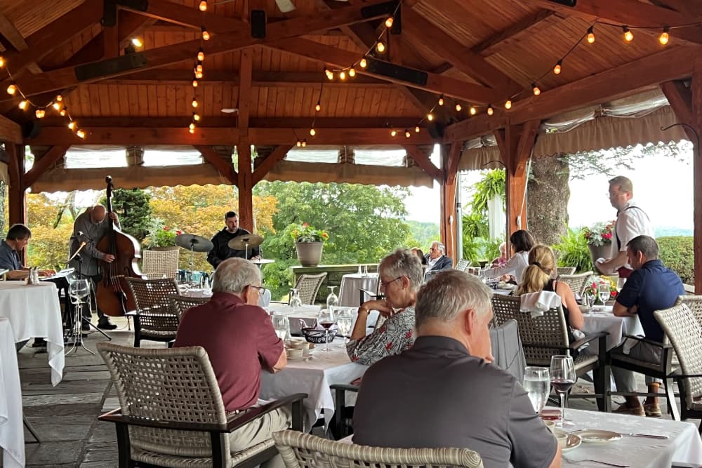 A band playing various instruments on a covered terrace with people dining at tables.