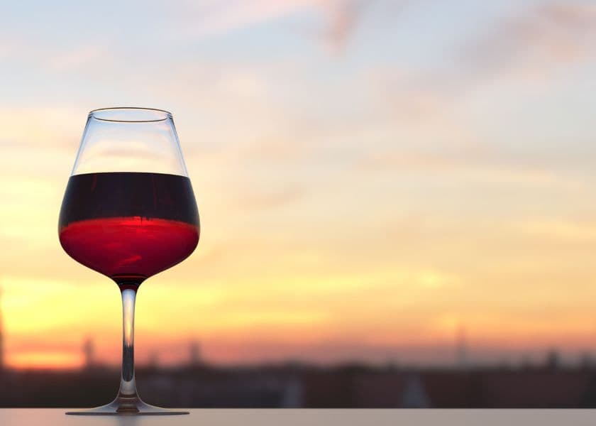 A glass of red wine against a colorful sunset.