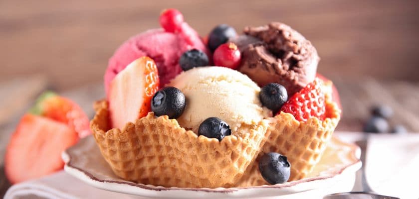 A waffle bowl filled with scoops of chocolate, strawberry, and vanilla ice cream, topped with fresh berries and strawberries.