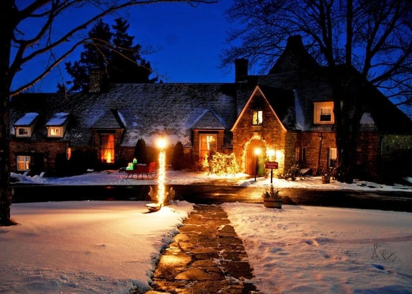 A beautifully lit stone house surrounded by snow under a twilight sky.