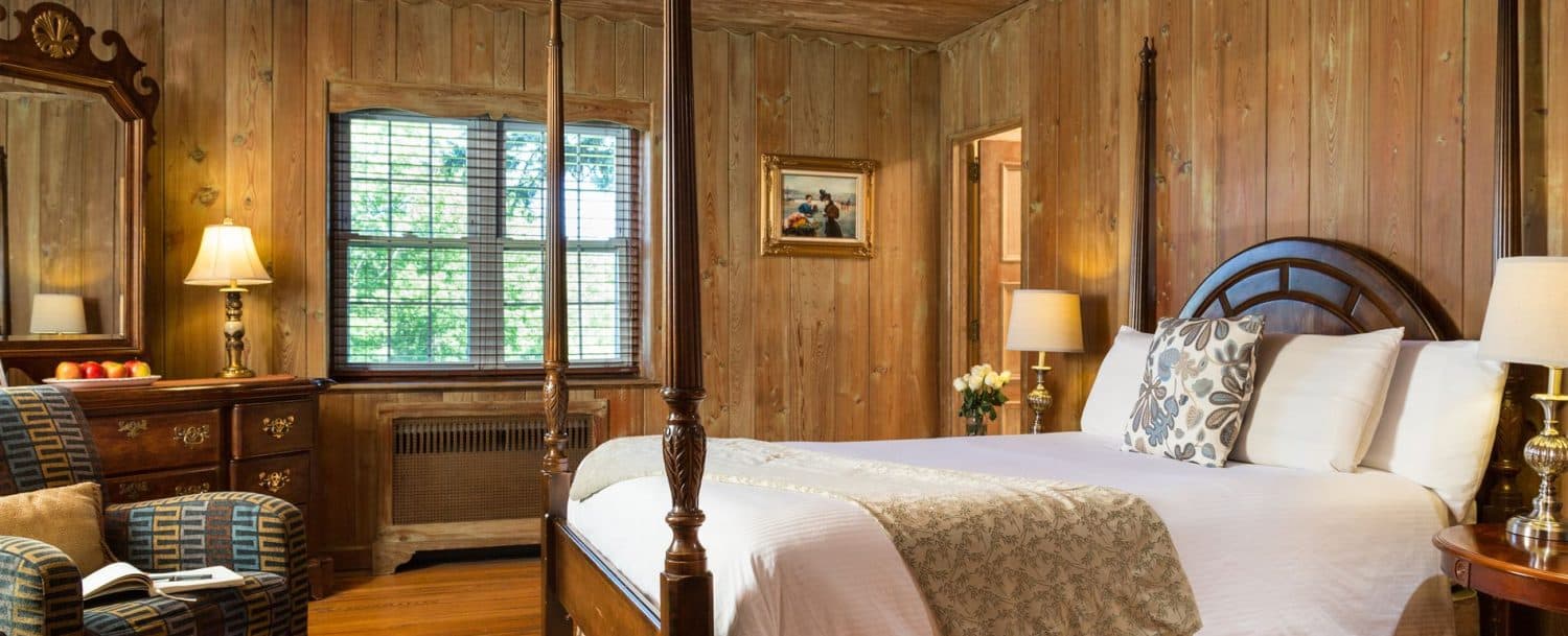 Cozy bedroom featuring a four-poster bed, wooden walls, and natural light from a window.