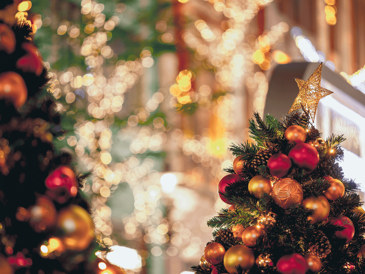 Close-up of a decorated Christmas tree with a star on top and blurred festive lights in the background.