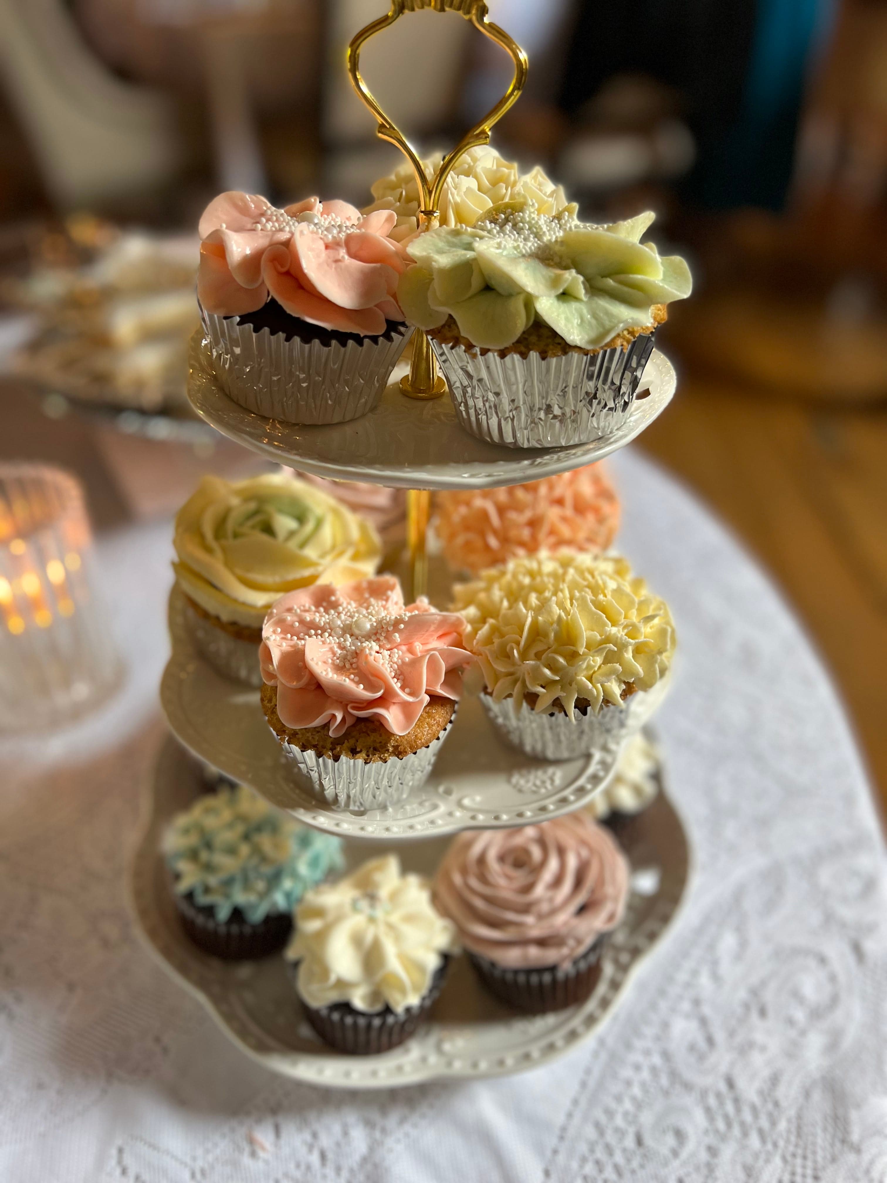 A white tiered stand displaying a variety of cupcakes with different colored frostings and decorations.