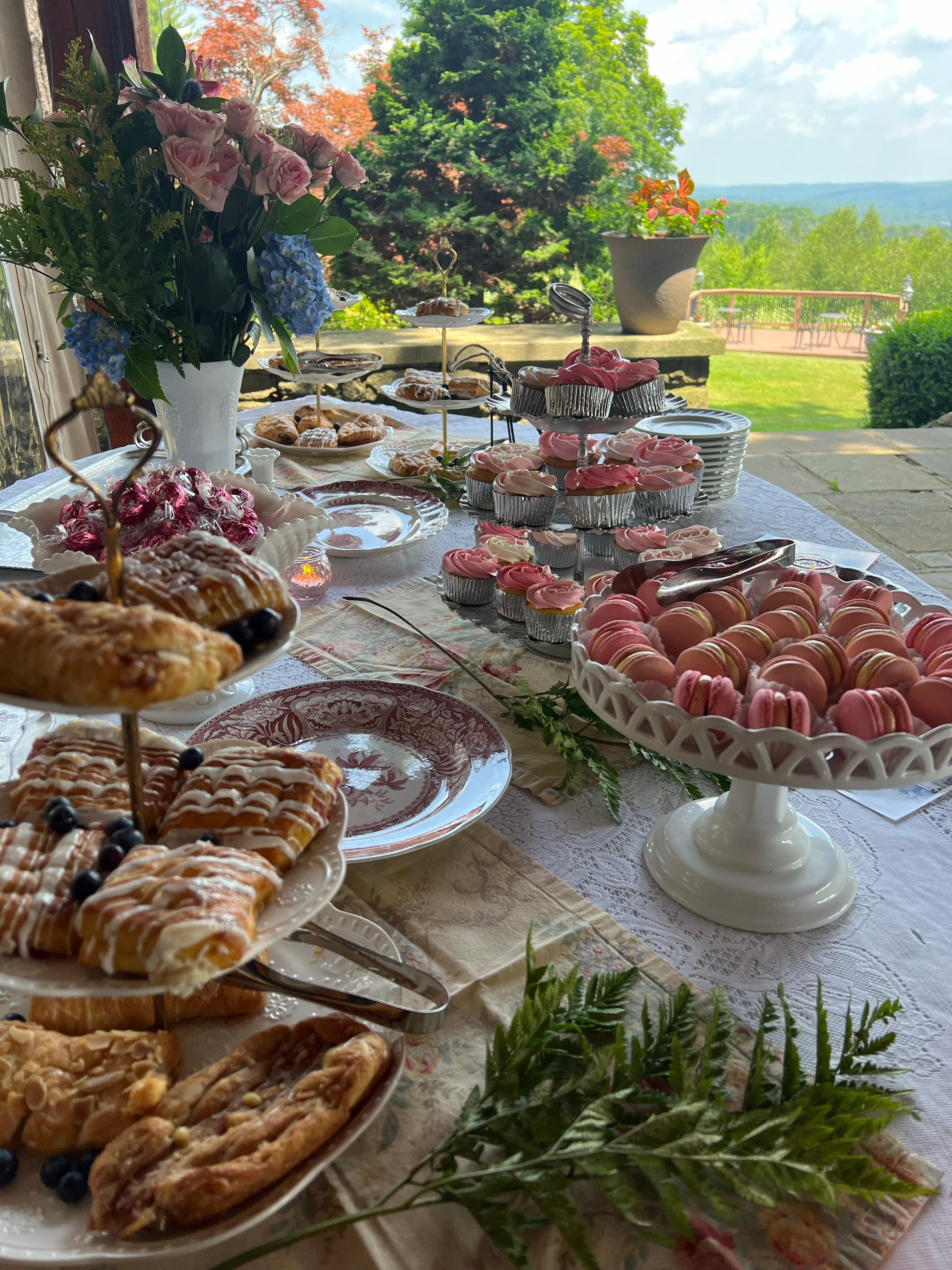 A charming outdoor tea party with a variety of pastries, flowers, and a stunning vista.