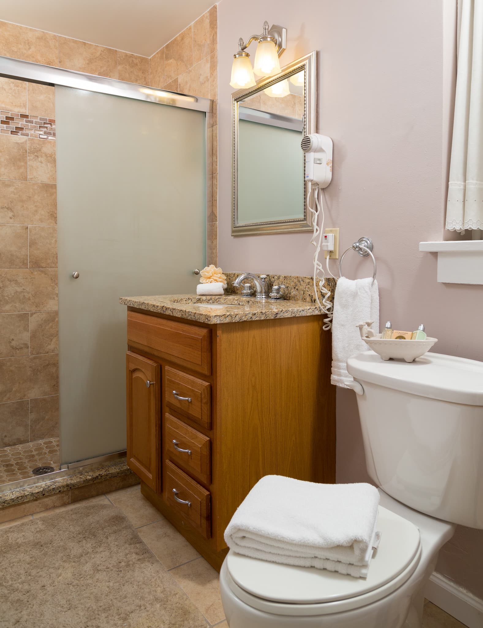 A clean bathroom featuring a shower, sink with wood cabinets, and a toilet.