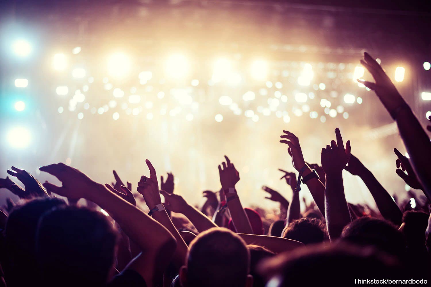 A crowd with raised hands enjoying a concert under bright stage lights.