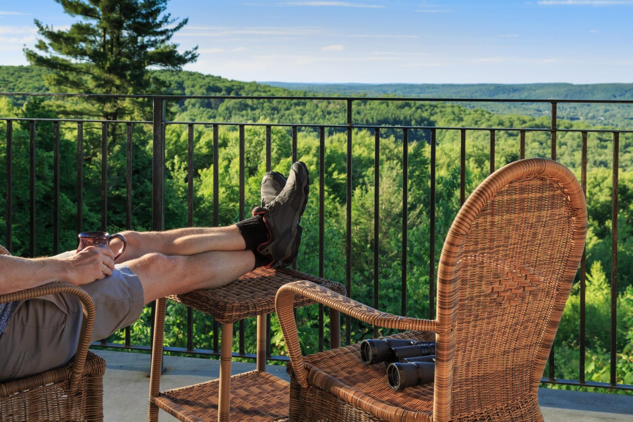 A person relaxes in a chair with feet up, overlooking a lush green landscape.