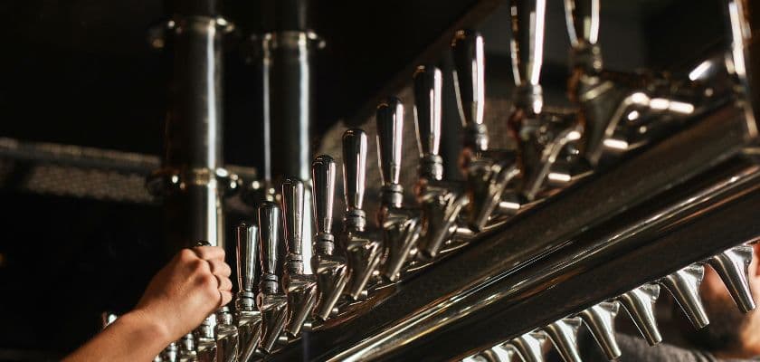 A row of shiny brewery taps behind a bar in a dimly lit brewery.