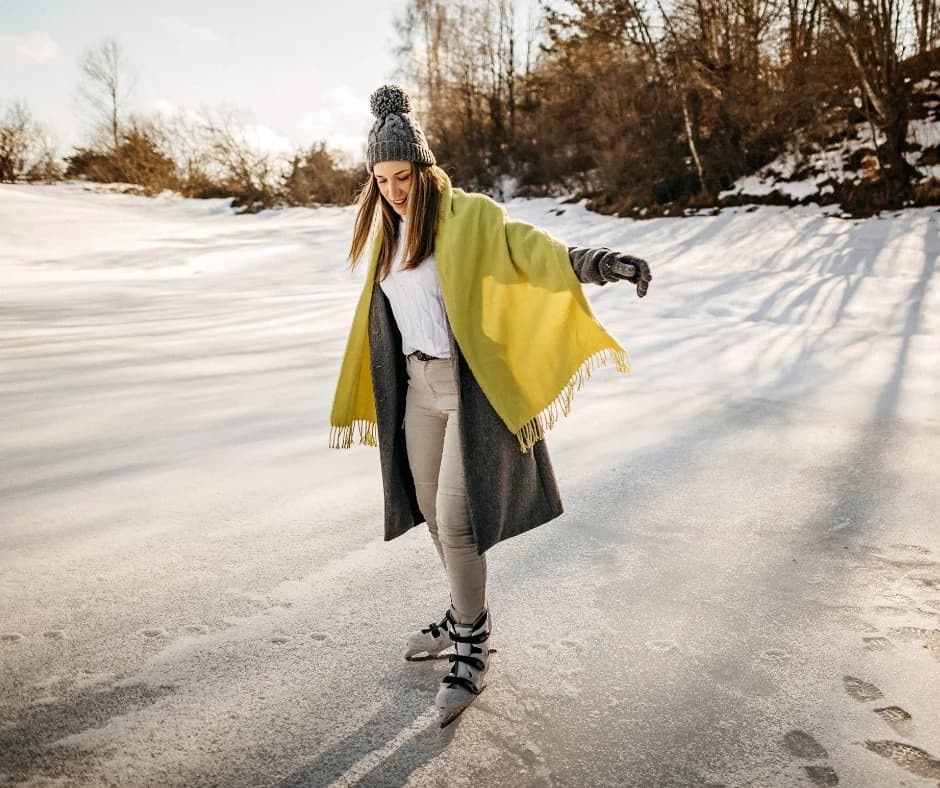 A woman skates on ice while wearing a warm outfit, including a green shawl and a knitted beanie.