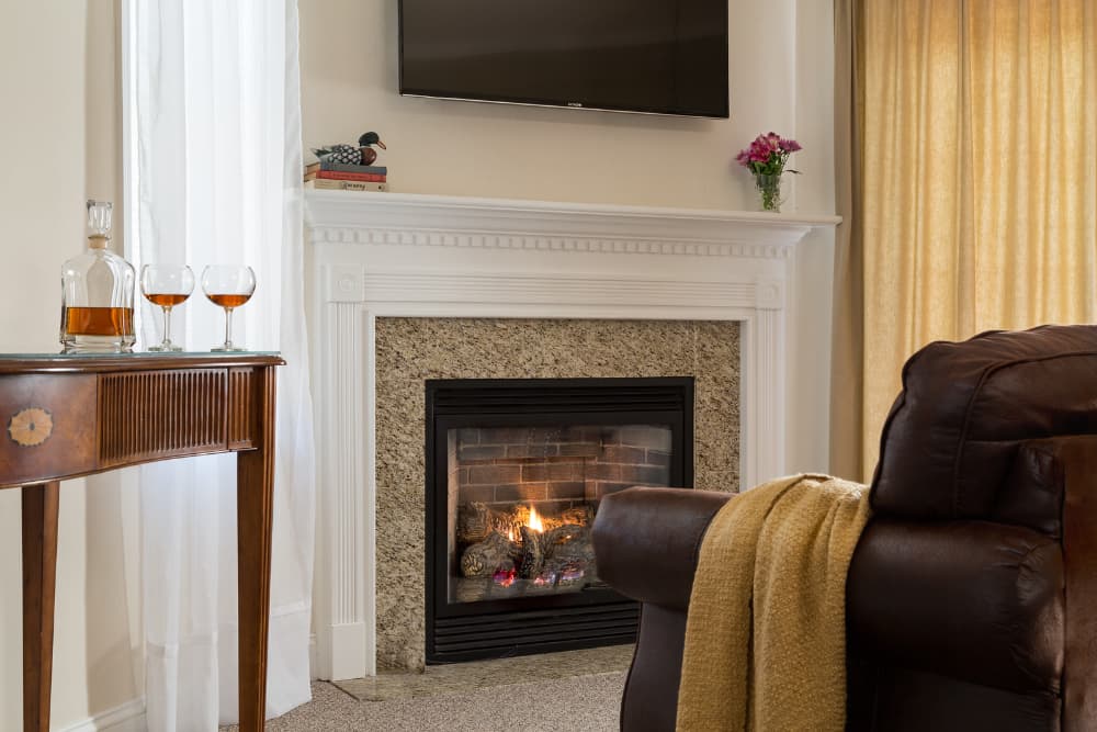 A living room with a fireplace, a leather armchair with a blanket, and a side table with glasses and a decanter.