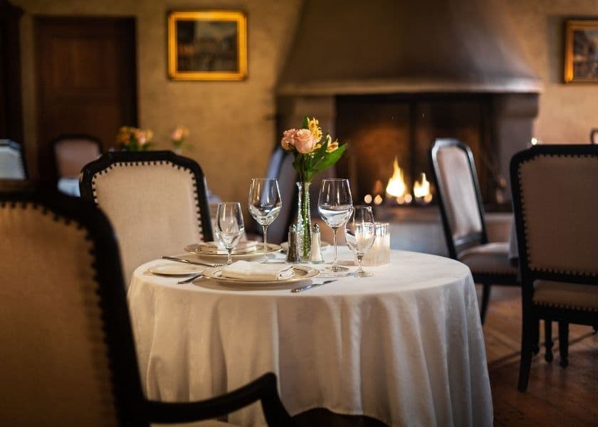 A elegantly set dining table with glassware and flowers in a cozy restaurant near a fireplace.