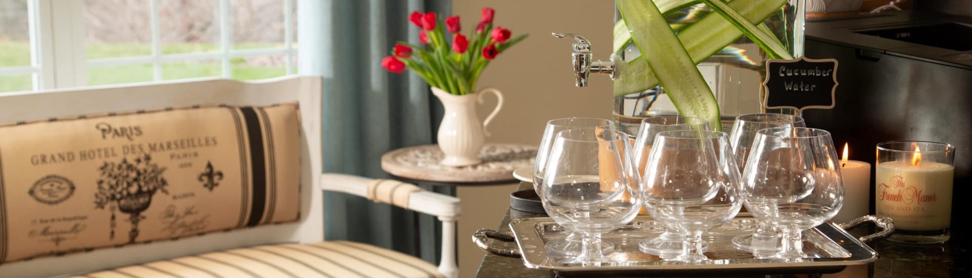 A cozy sitting area with a vase of red tulips, a tray of glasses, and a dispenser with cucumber water.