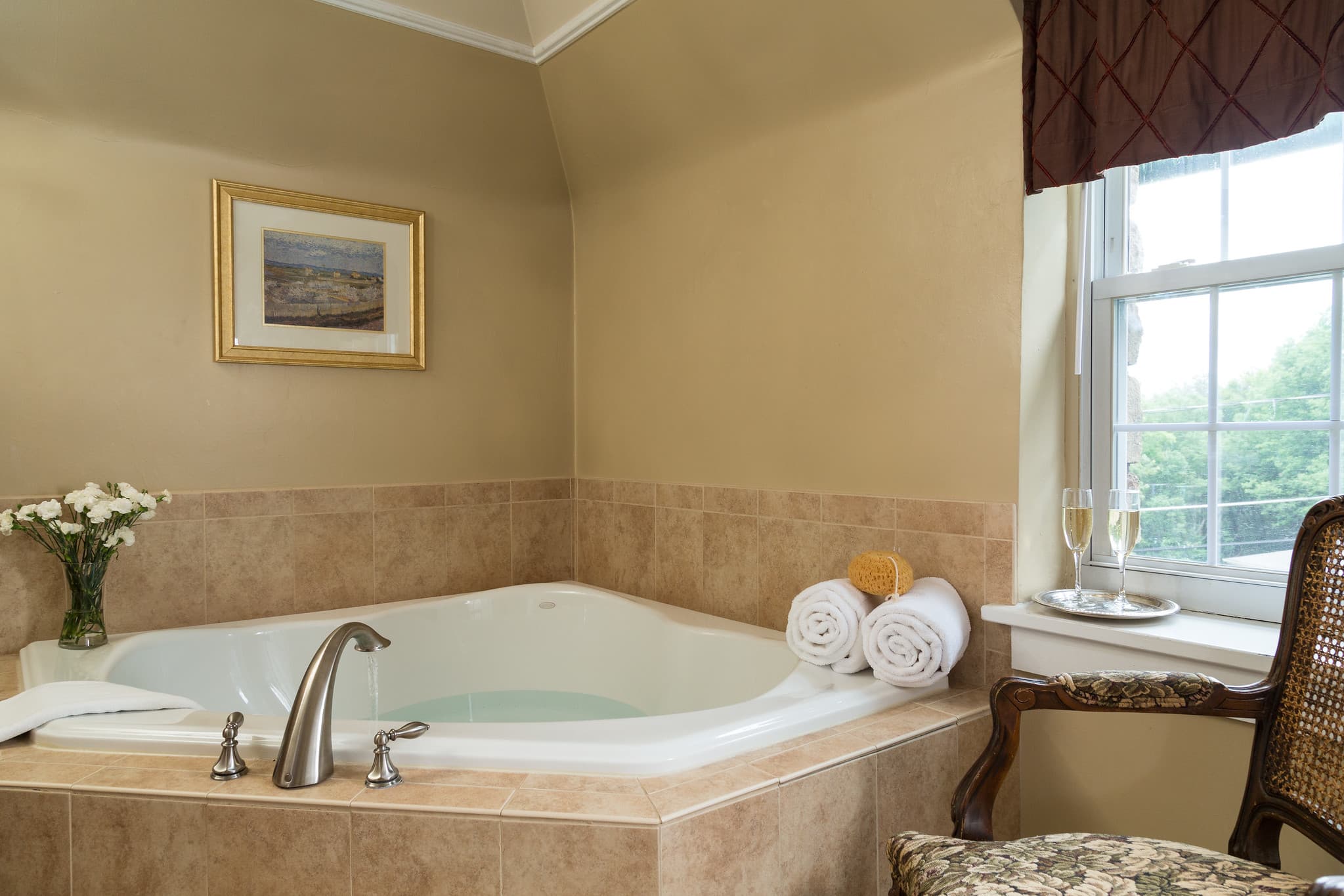 A luxurious corner bathtub with towels and champagne beside a window in a cozy room.