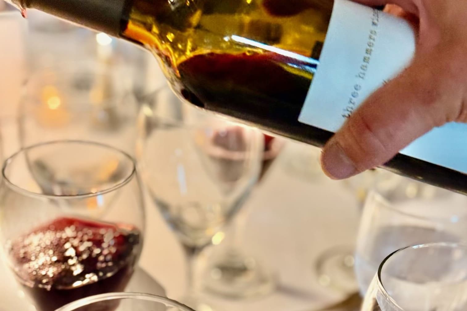 A hand pours wine from a bottle into glasses on a table.