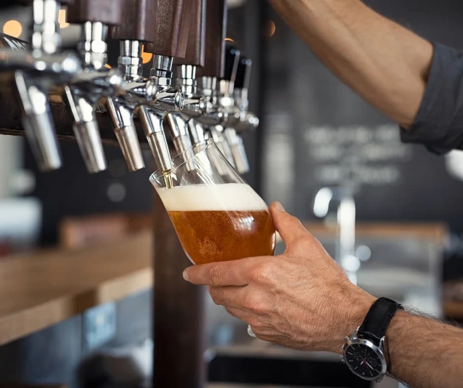 A hand pours a frothy beer into a glass from a tap.