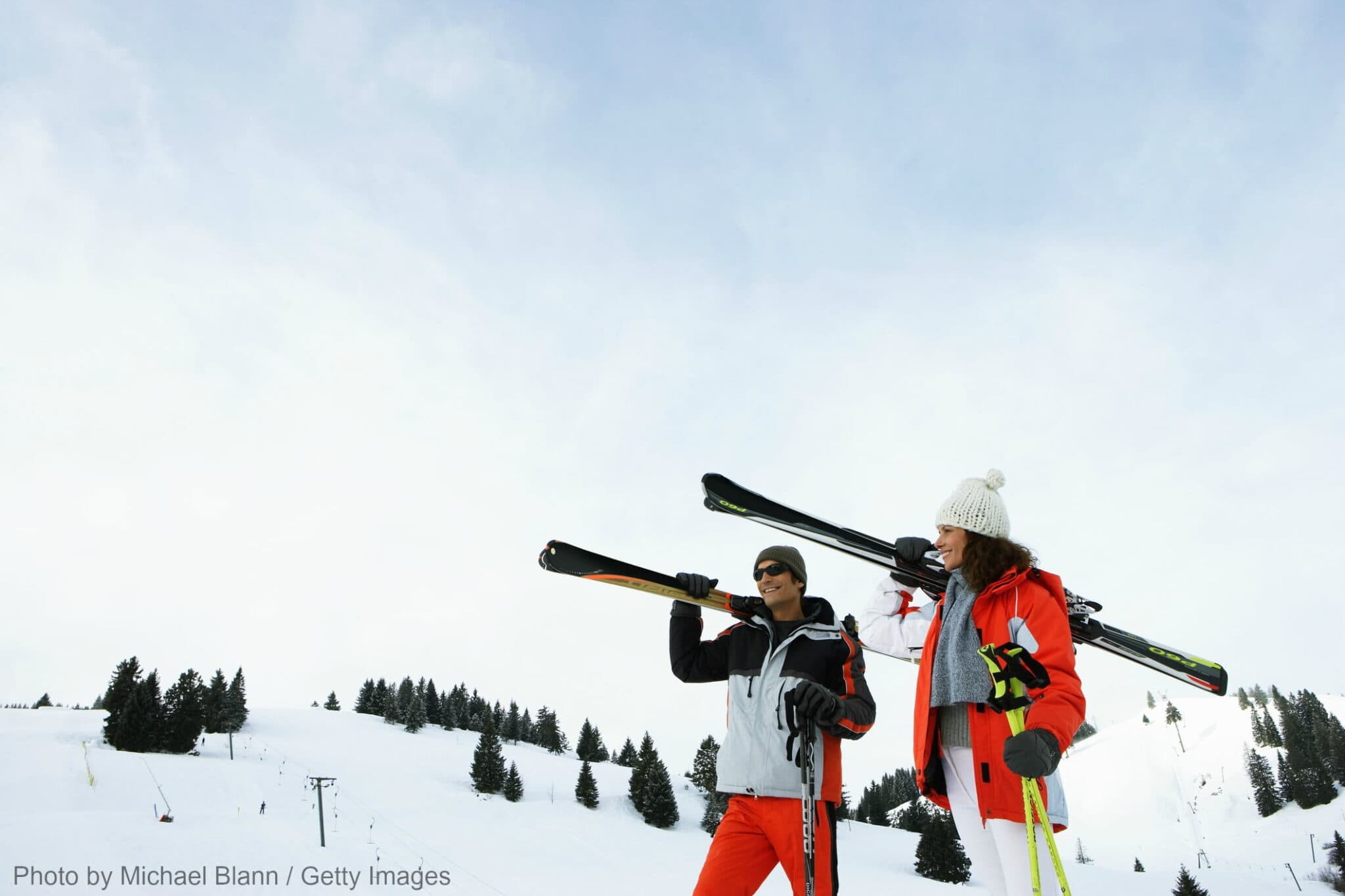 Two skiers carry their skis while standing on a snowy slope.