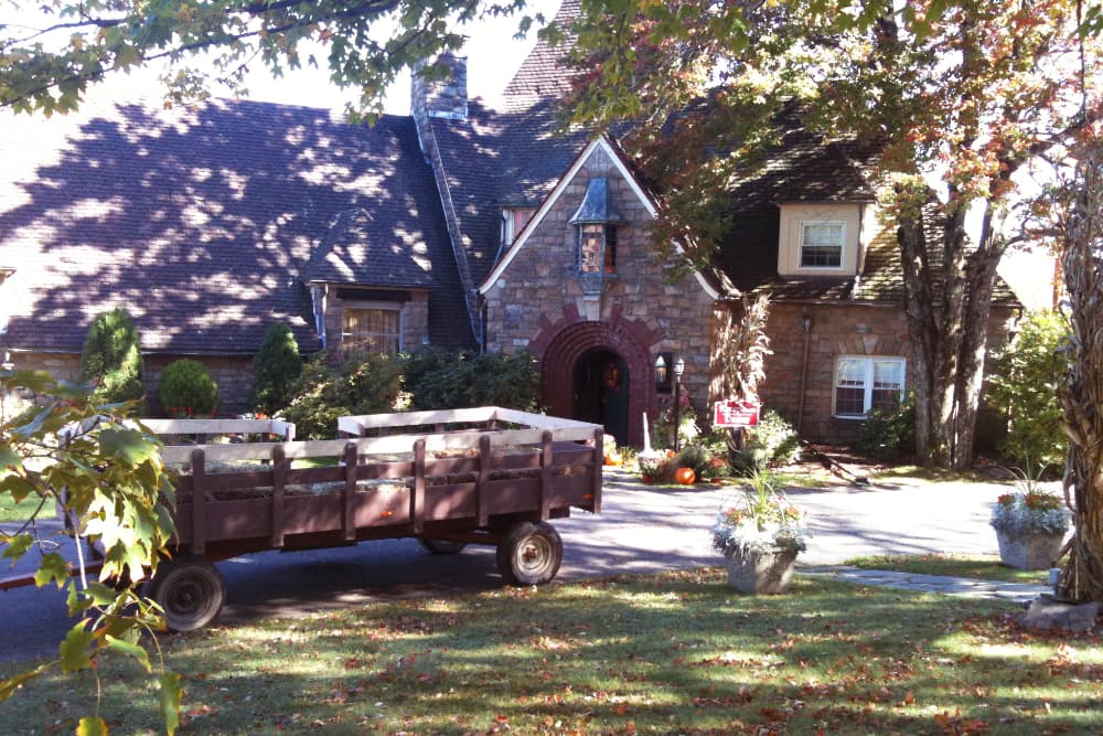 A historic stone building with a large wagon ready for a hayride in the foreground, surrounded by autumn foliage.
