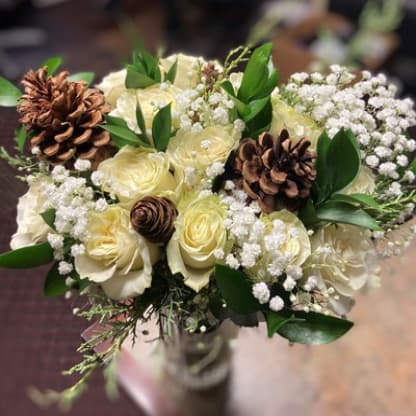 A beautiful bouquet featuring white roses, baby's breath, greenery, and pine cones.