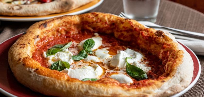 A close-up of a margherita pizza topped with mozzarella and fresh basil on a red plate.