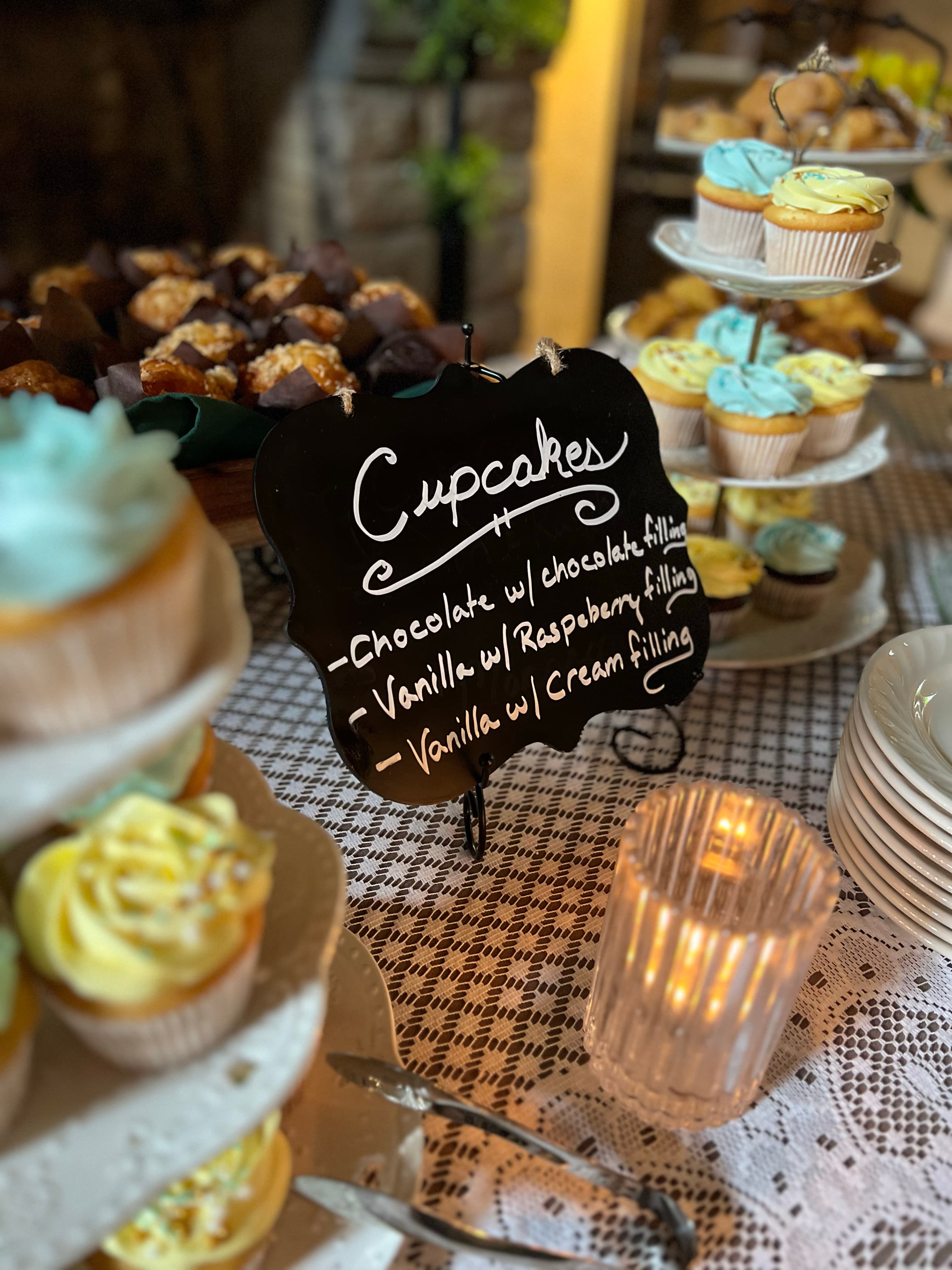 A buffet table filled with cupcakes in various flavors, including chocolate with chocolate filling, vanilla with raspberry filling, and vanilla with cream filling.