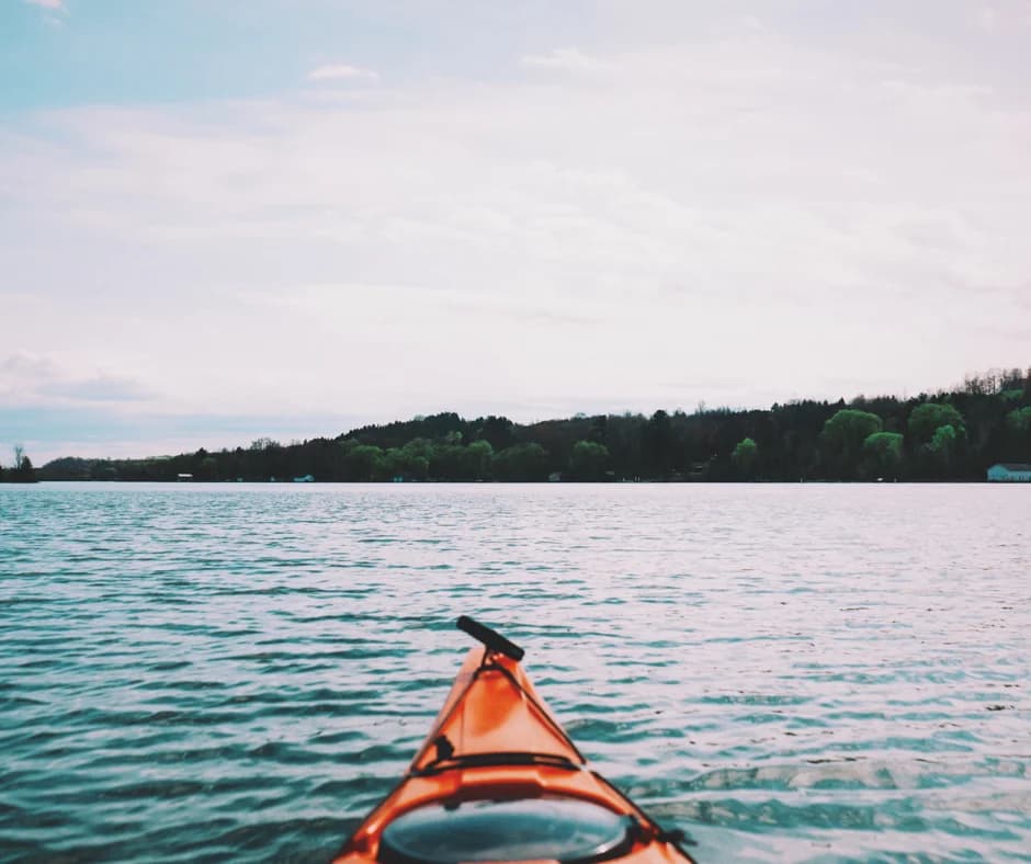 View from an orange kayak on a calm lake with lush green hills in the background.