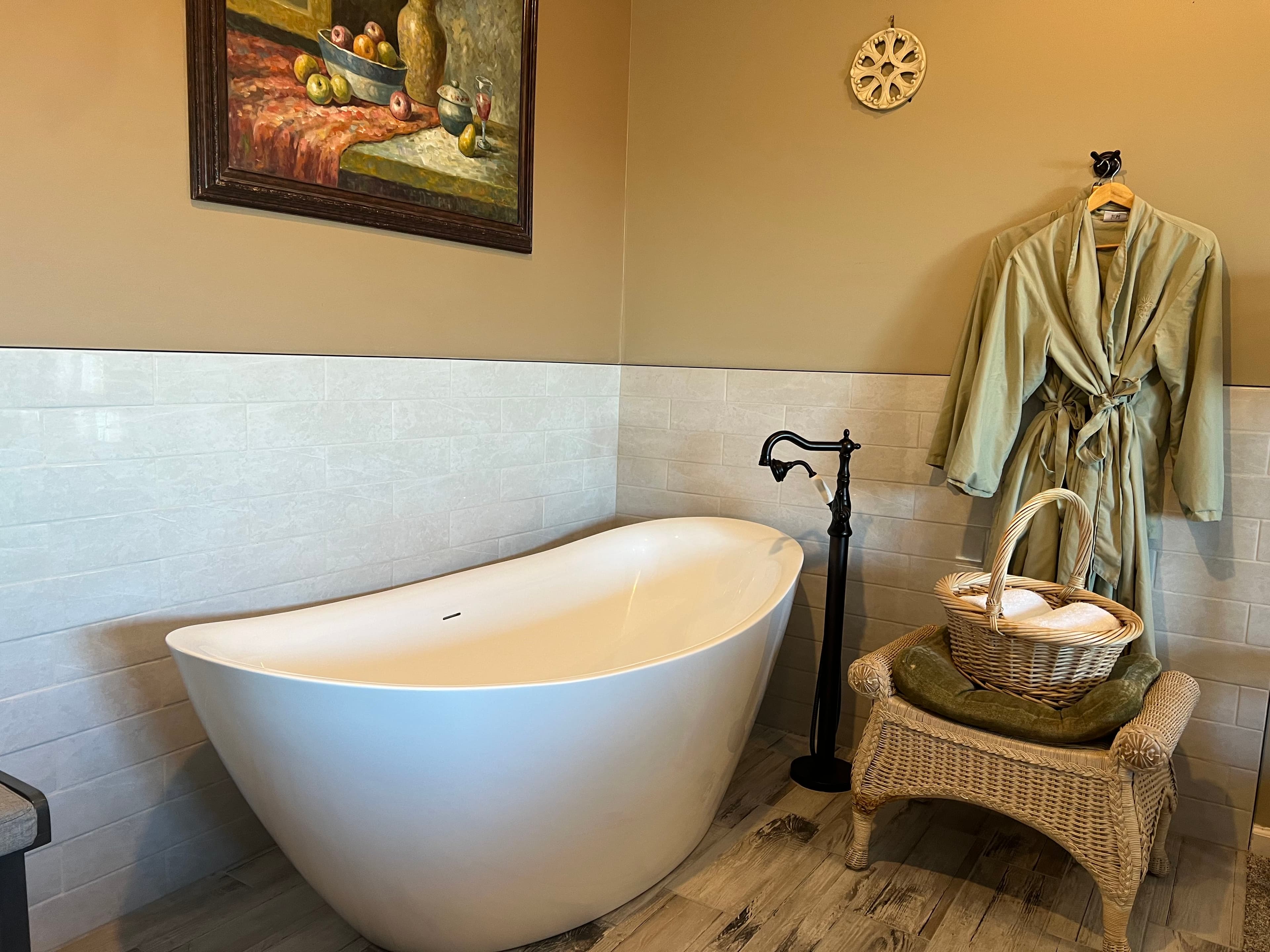 A cozy bathroom featuring a freestanding white bathtub, a green robe hanging on the wall, and a wicker basket with towels.