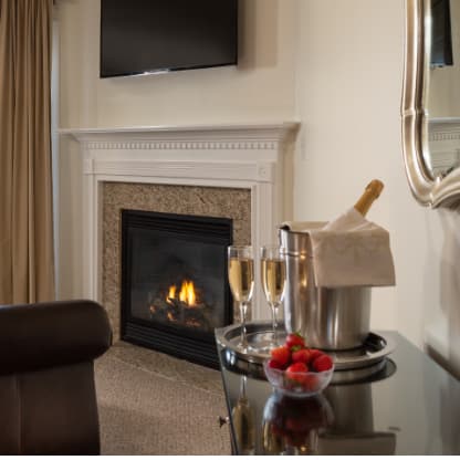 A cozy living room with a fireplace, a champagne bucket with glasses, and a bowl of strawberries on a tray.