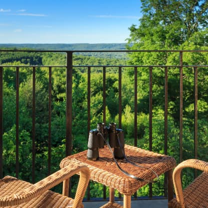 A balcony with wicker chairs, a small table, and binoculars overlooking the Poconos mountains.