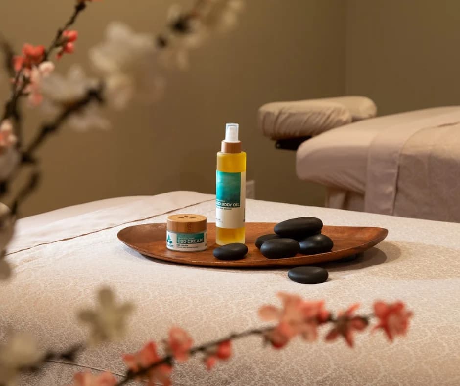 A calming spa setting featuring massage oils, stones, and a cream on a wooden tray.