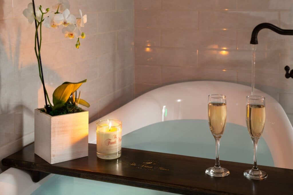 A serene bathtub setting with two glasses of champagne, a lit candle, and an orchid plant.