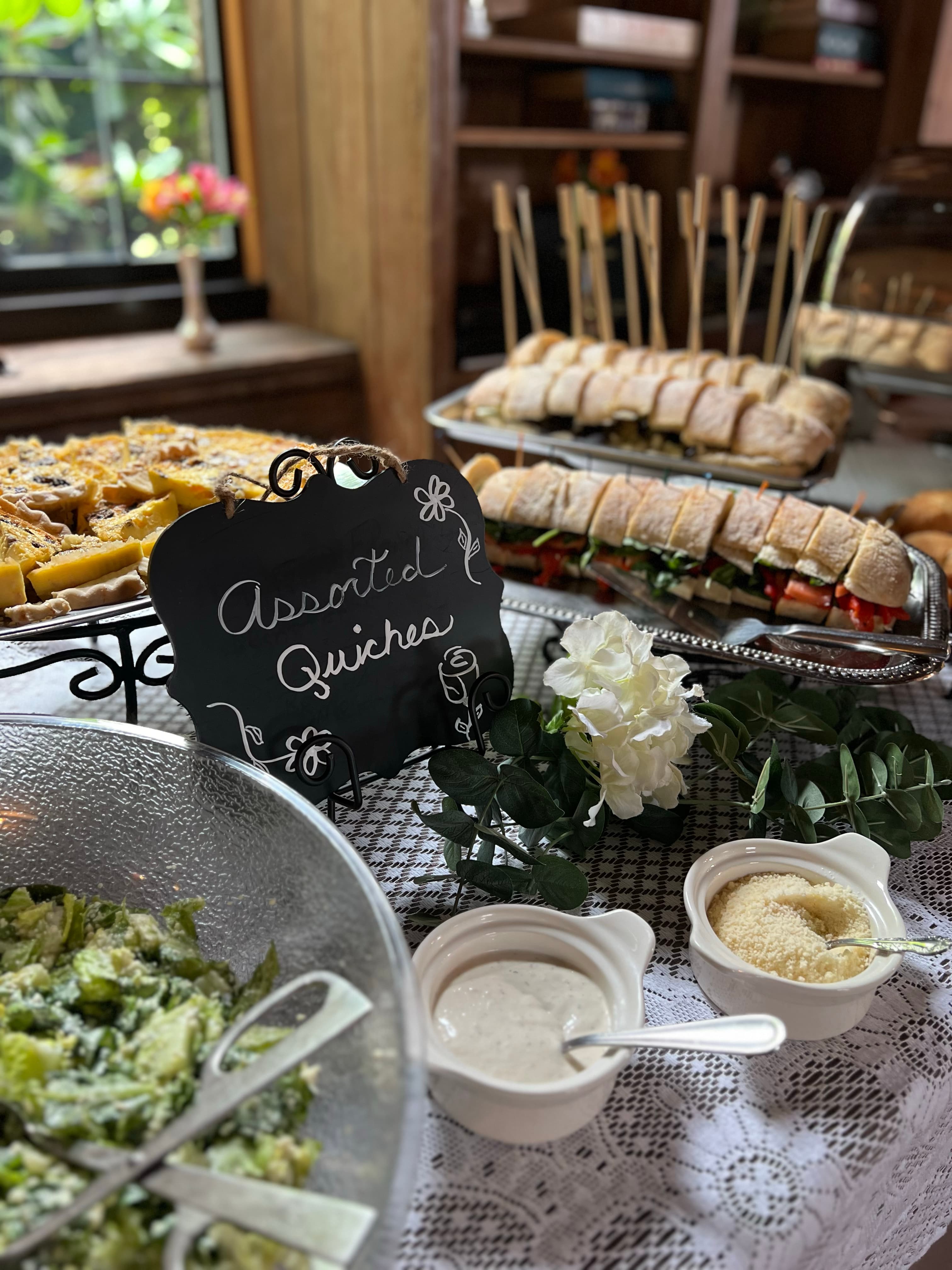 A buffet table with assorted quiches, sandwiches, salad, and other finger foods.