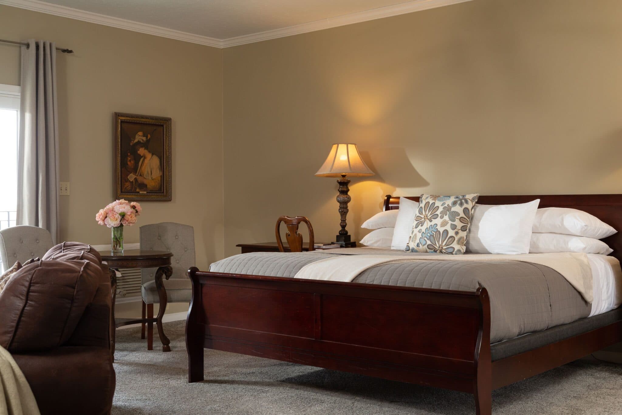 A cozy bedroom with a wooden bed, soft lighting, and a small table with flowers.