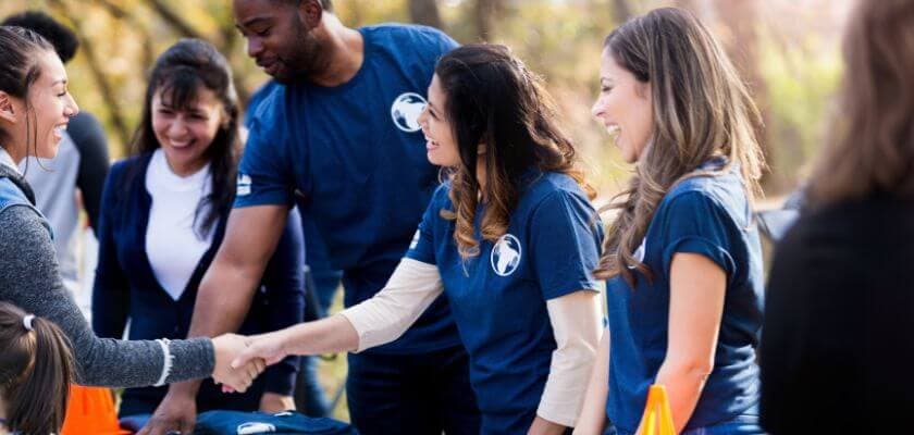 A group of people in blue shirts engaging in friendly conversation and shaking hands outdoors.