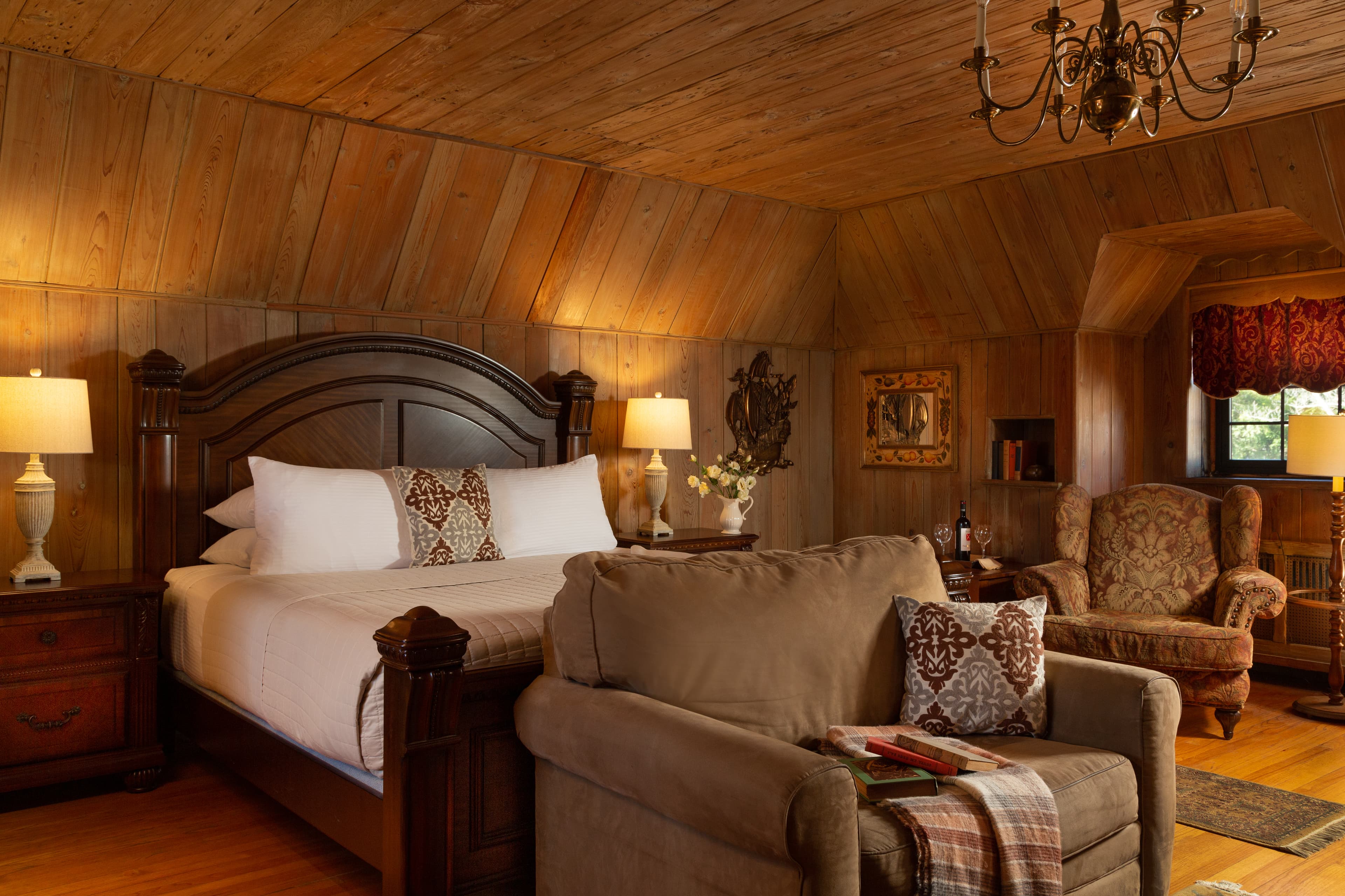 Cozy rustic bedroom featuring a wooden panelled ceiling, a large bed, and comfortable seating.