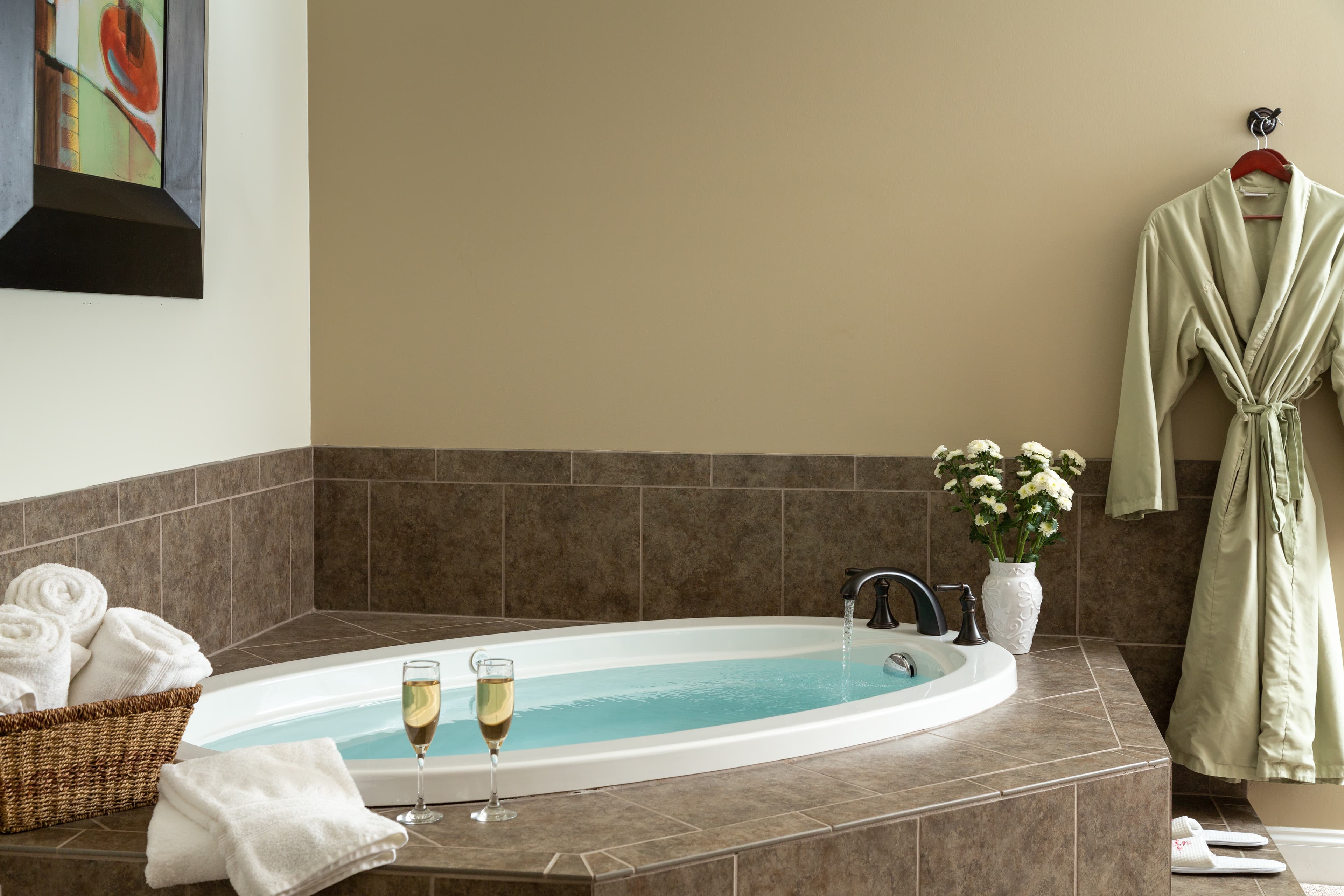 A cozy bathroom featuring a jetted tub, two flutes of champagne, plush towels, and a soft bathrobe.
