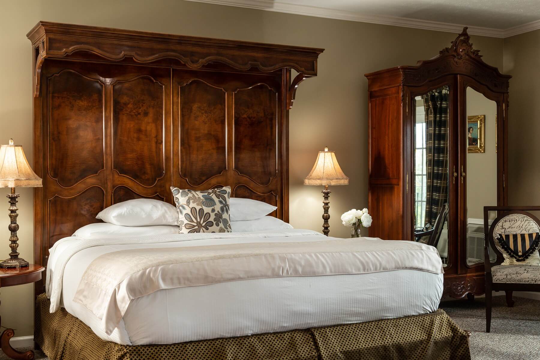 A cozy bedroom featuring a large wooden bed with an ornate headboard, elegant lamps, and antique furnishings.