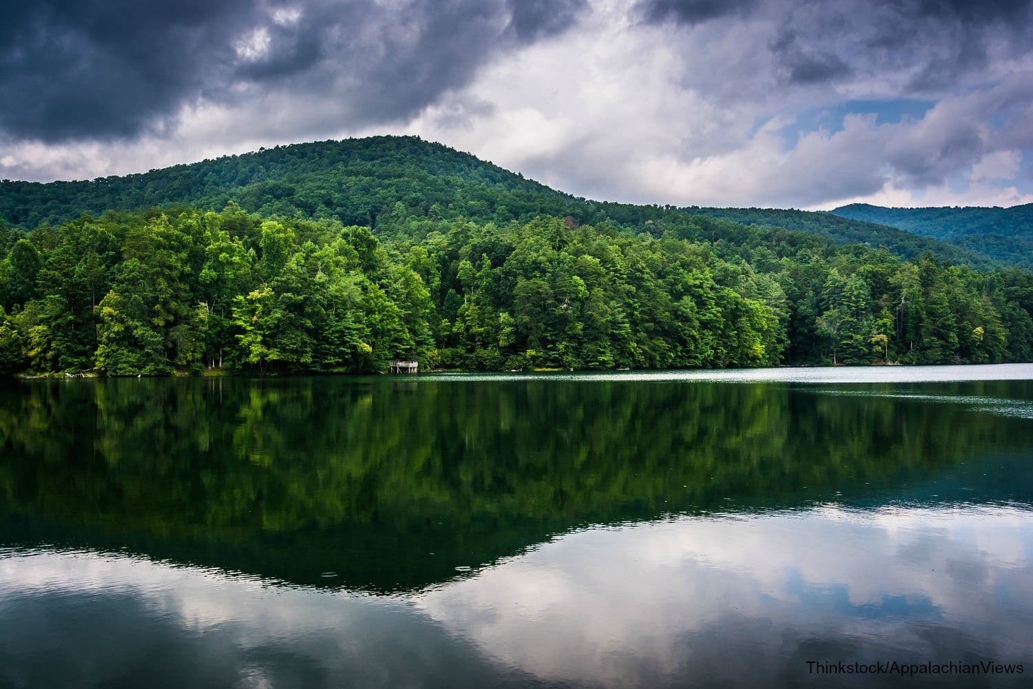 A tranquil lake reflects green hills and an overcast sky.
