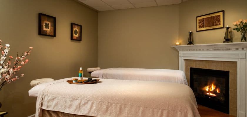 A serene spa room featuring two massage tables, calming decor, and a cozy fireplace.