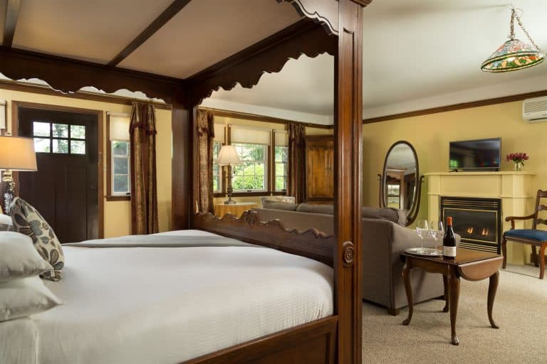 Cozy bedroom featuring a four-poster bed and a sitting area with a fireplace and windows.