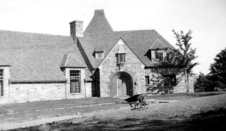 A historic photo of the French Manor Inn, a stone building with a wheelbarrow in the foreground.