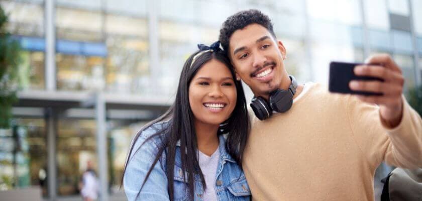 A smiling couple takes a selfie outdoors.