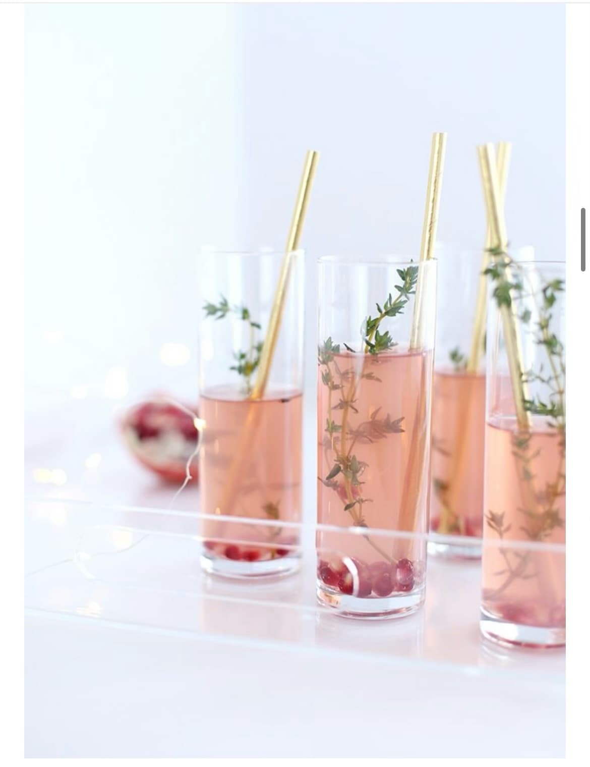 Several tall glasses with a pink beverage, fresh raspberries and thyme sprigs, and gold straws.