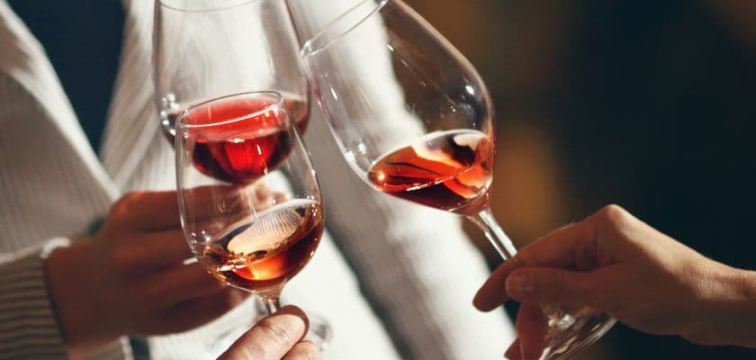 Three wine glasses filled with red wine are clinking together in celebration.