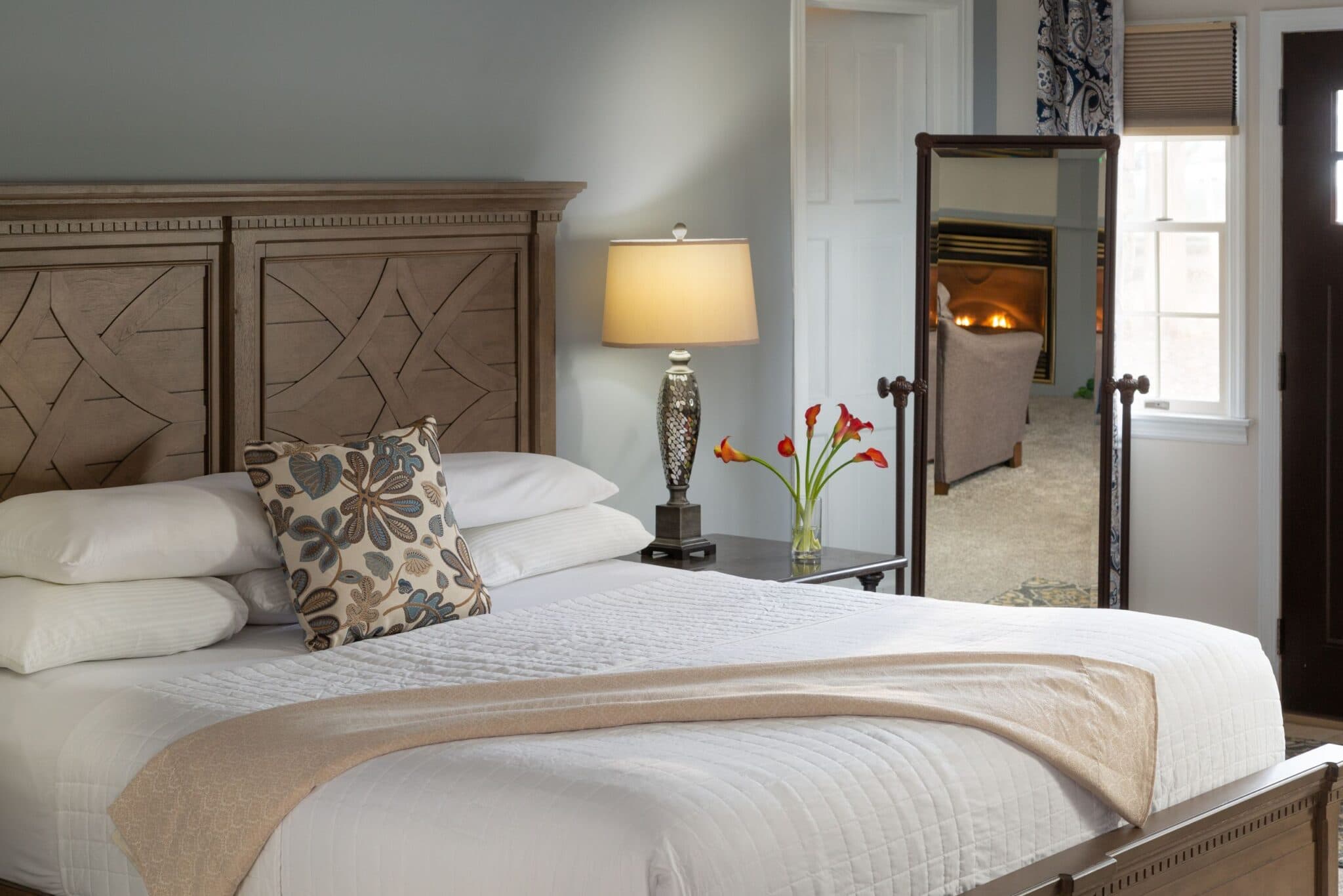 A cozy bedroom featuring a wooden bed with a decorative pillow, a bedside lamp, and a vase of flowers.