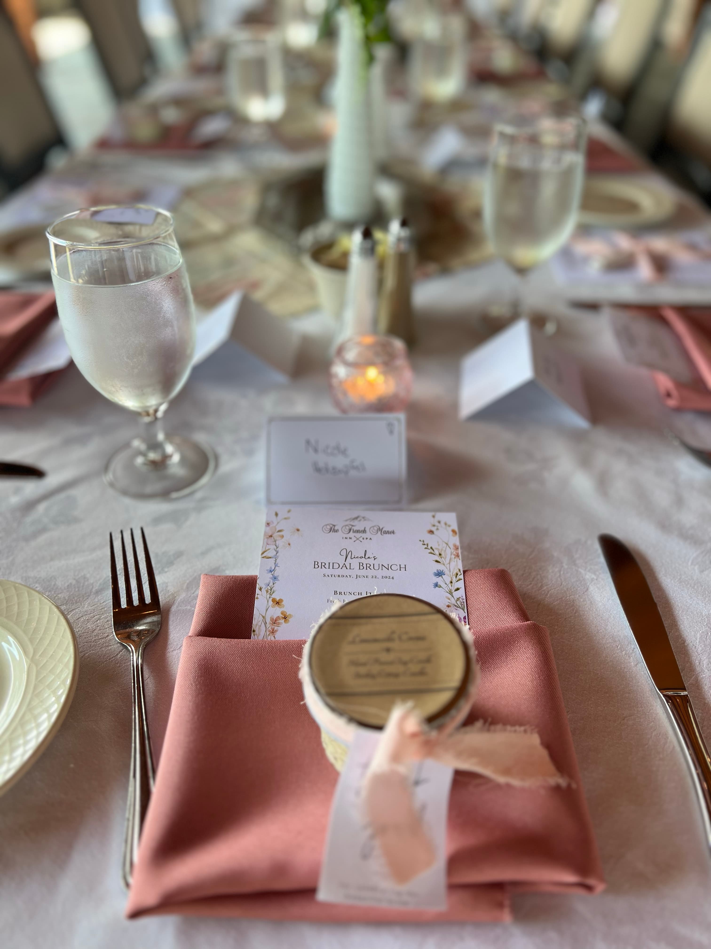 A beautifully set table for a bridal brunch, featuring a peach-colored napkin, a glass of water, and a place card.