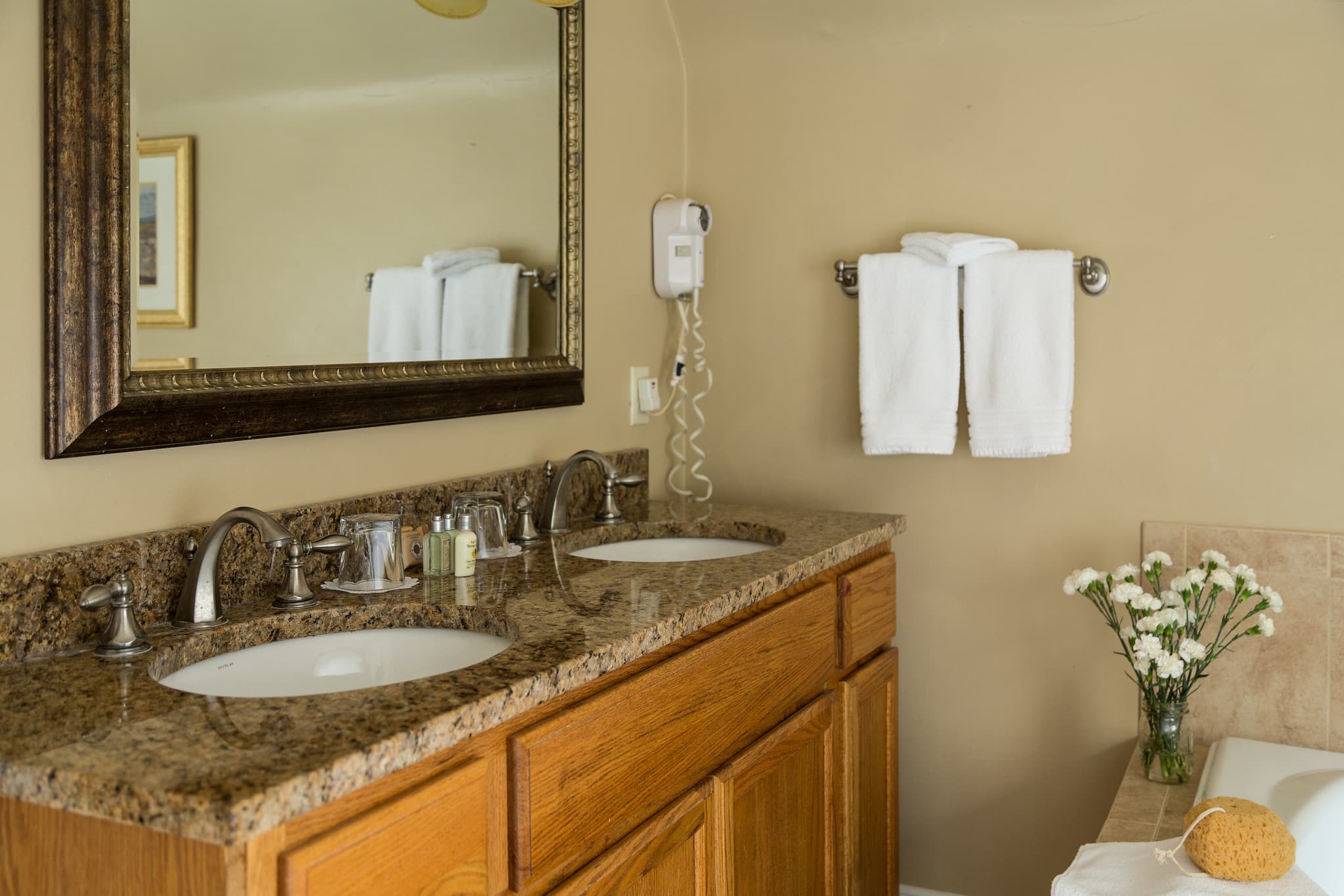A well-lit bathroom featuring a double vanity with a granite countertop, two sinks, and neatly hung white towels.