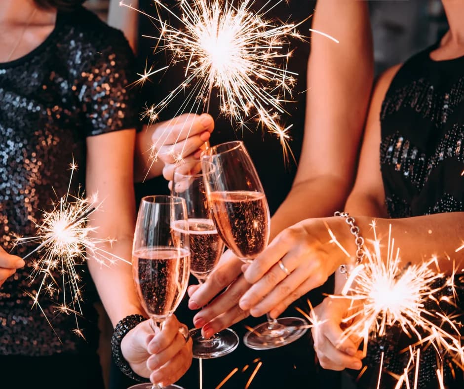 Four hands clinking champagne glasses with sparklers in celebration.