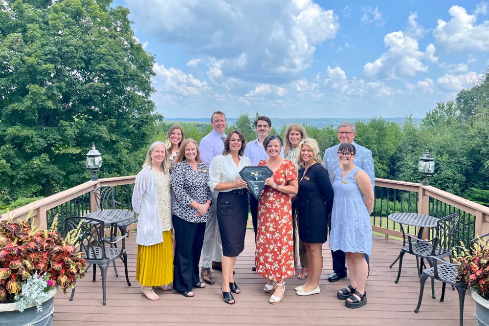 A group of people standing on a wood deck in front of trees and mountains receiving the AAA Award of Excellence for 2024.