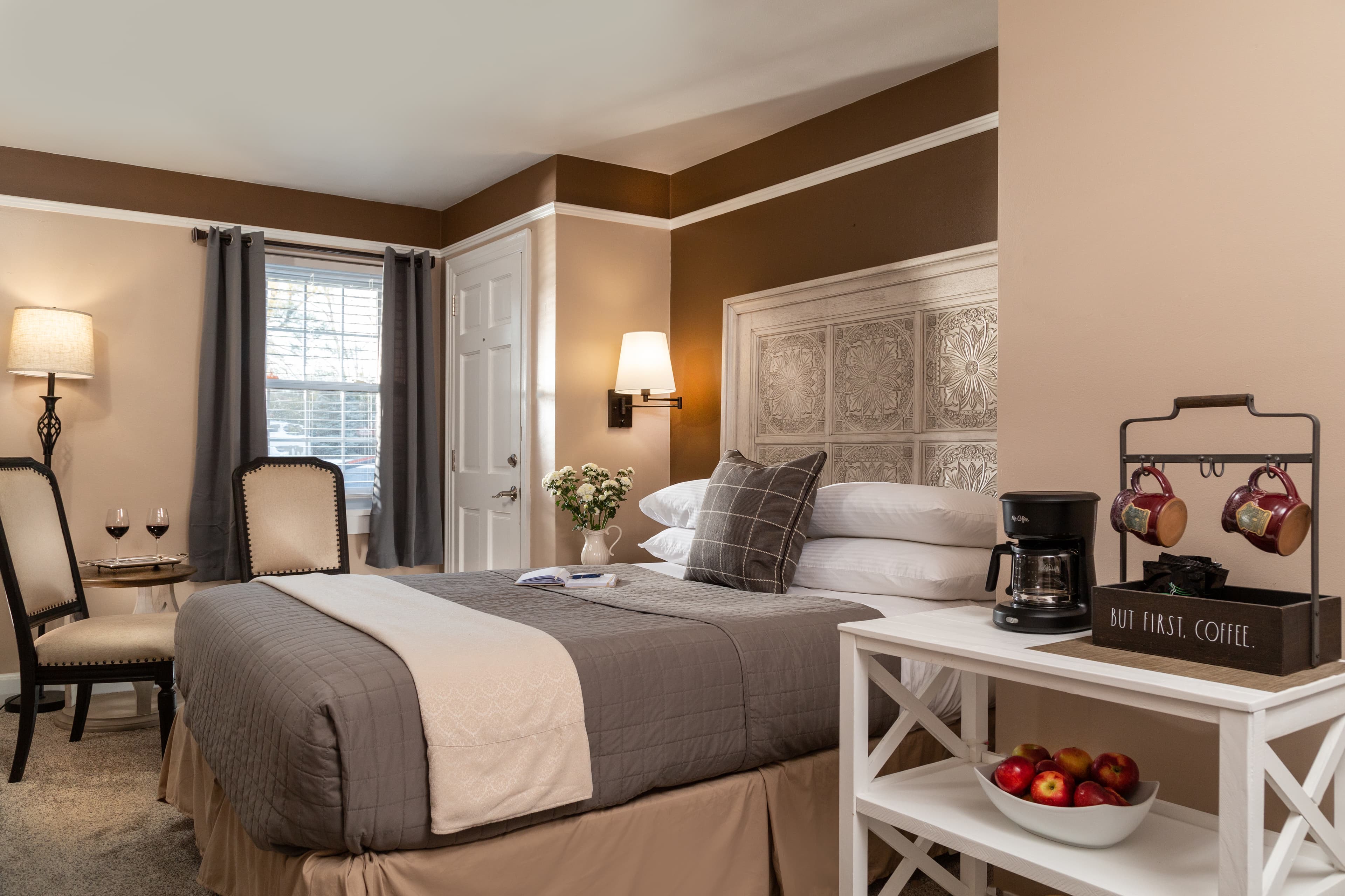 Cozy bedroom featuring a stylish bed, seating area, and coffee station with apples.